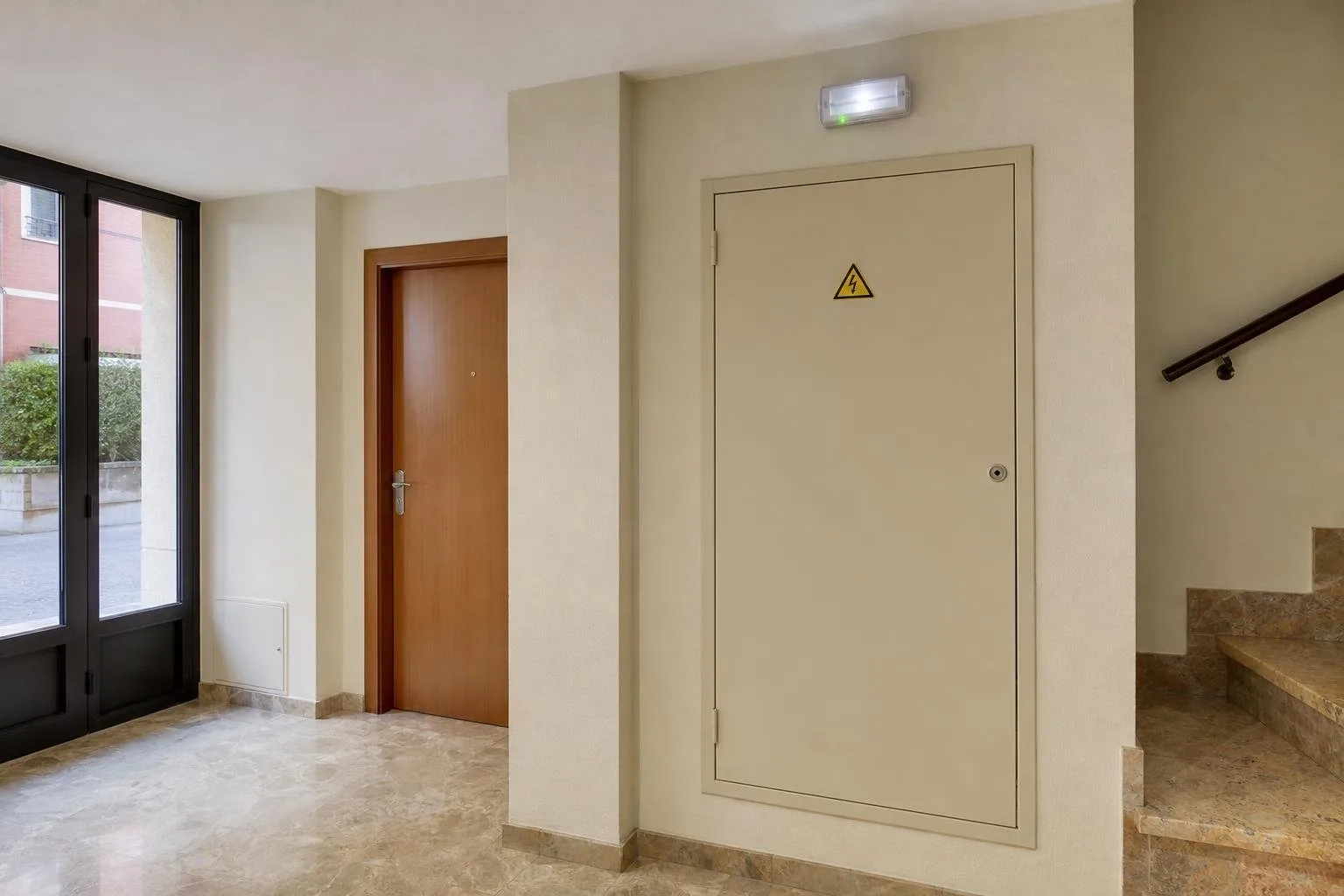 Portal de un edificio con luz de emergencia y armario eléctrico